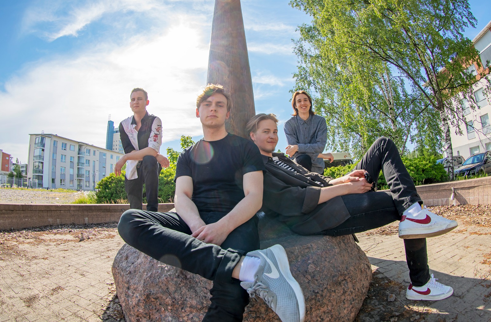 Kuva nelihenkisestä bändistä suuren patsaan juurella istumassa.