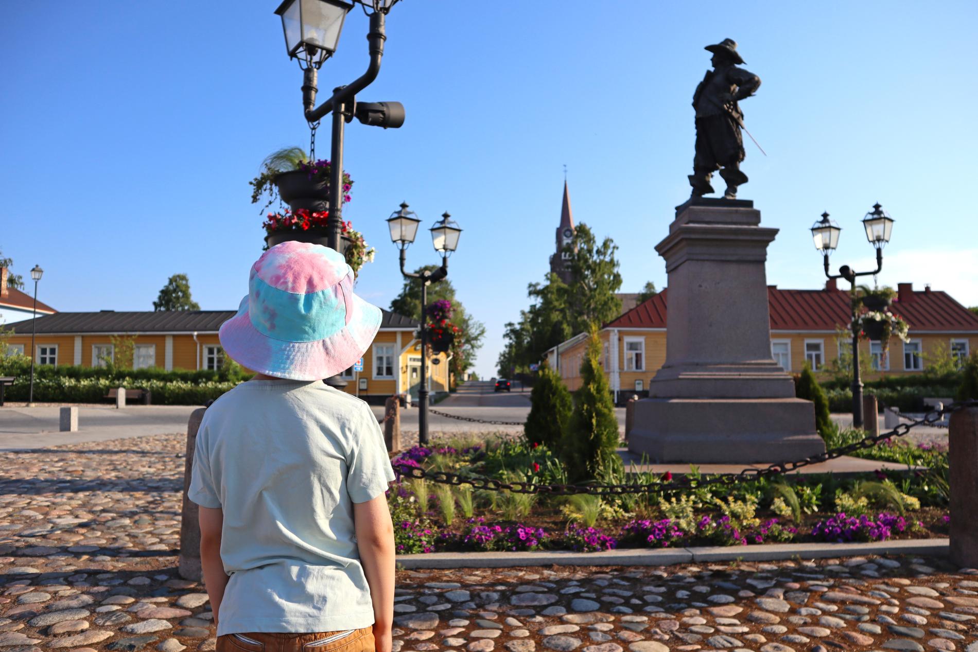 Hattupäinen poika katsoo kirkolle päin kesäisellä Pekkatorilla.