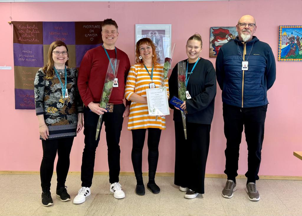 Kuvassa viisi ihmistä seisomassa vaaleanpunaisen seinän edessä.