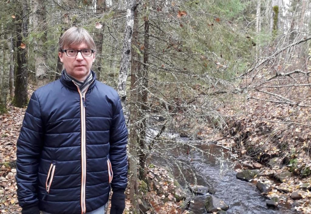 Harri Tuomela. Silmälasipäinen mies seisoo sinisessä ulkoilutakissaan metsässä.