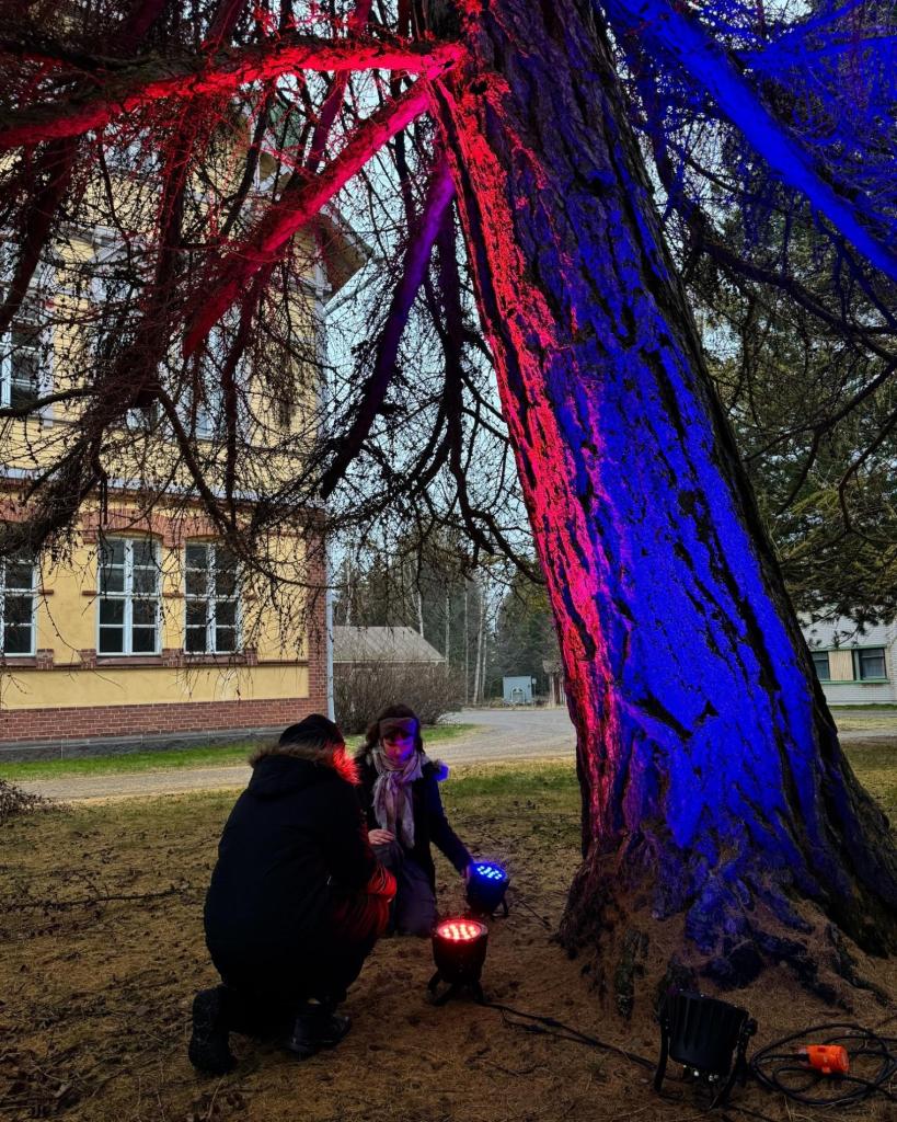 Kaksi henkilöä valmistelemassa installaatiota puiden katveessa.