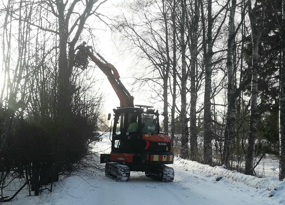 Kaivuri energiakouran kera siistii tien viereltä risuja.