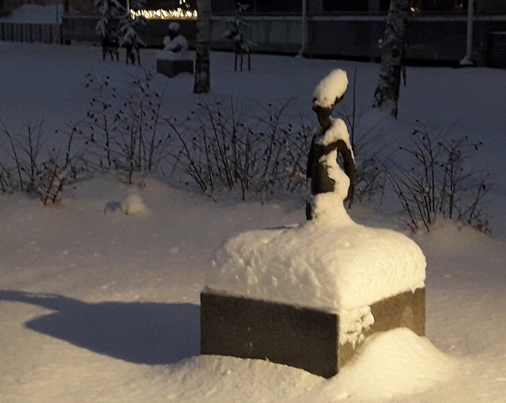 Veistospuiston valaistu patsas lumen peittämänä.