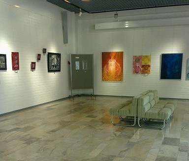 Tauluja vaaleilla seinillä, edessä sohvaryhmä.