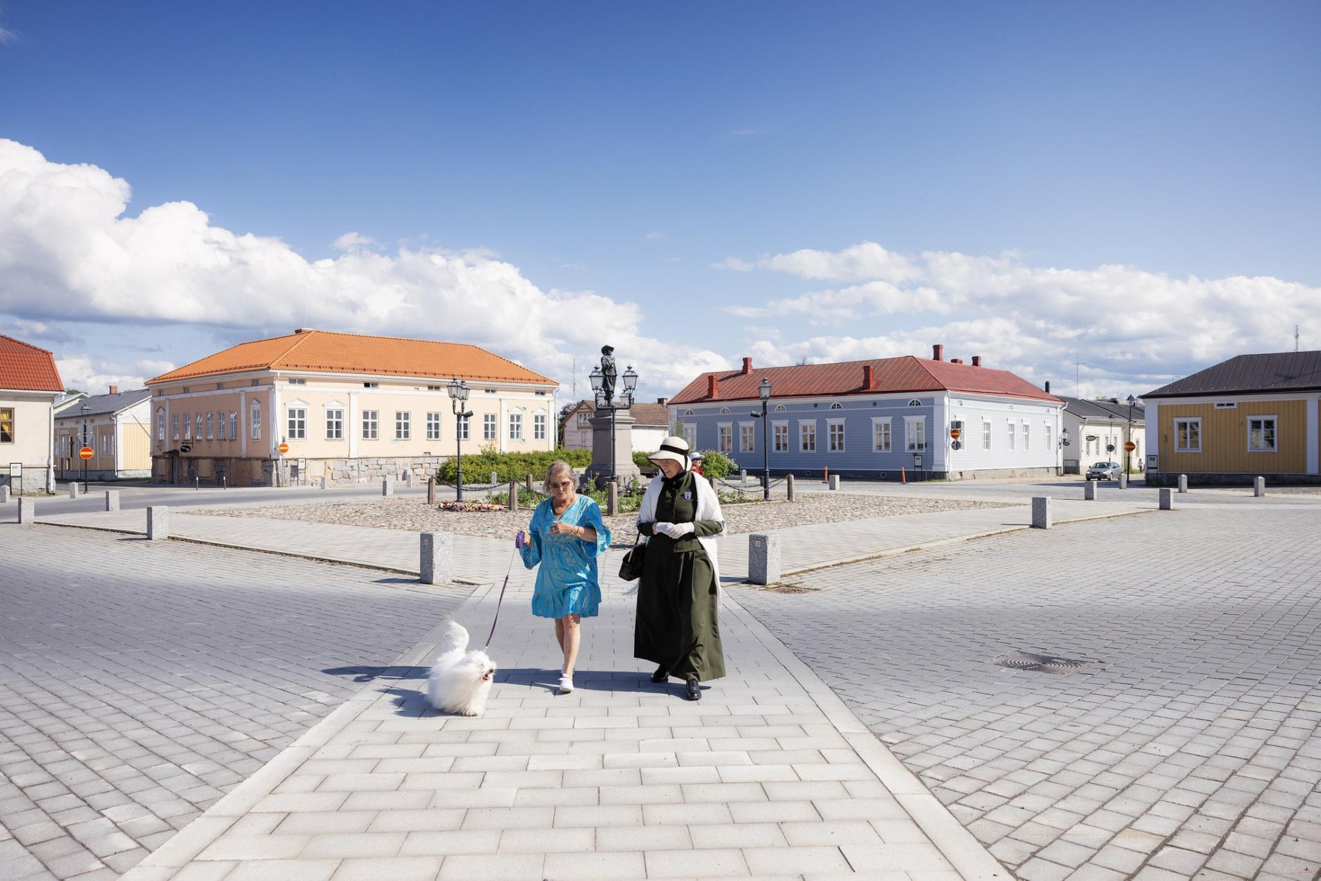Two people and a dog at Pekkatori square in summer.