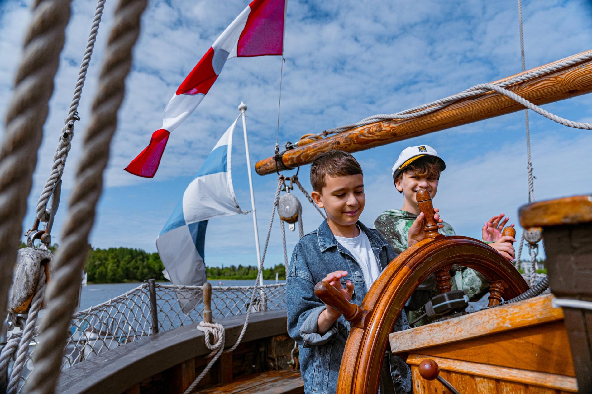 Kaksi lasta ohjaamassa ruoria perinnealuksella.