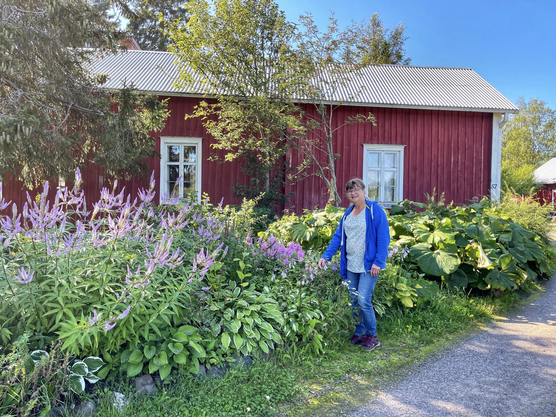 Tita in front of her red cottage in her home garden.