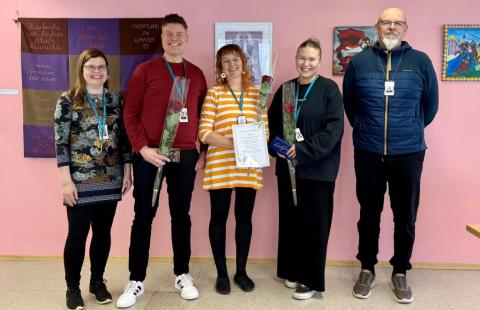 Kuvassa viisi ihmistä seisomassa vaaleanpunaisen seinän edessä.