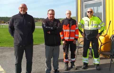 Neljä ihmistä seisoo rivissä jäteaseman toimistorakennuksen ulkopuolella.