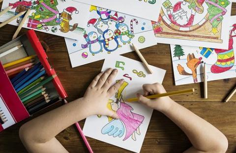 Lapsen piirustuksia pöydällä. Lapsen kädet värittävät yhtä piirrosta.