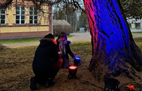 Kaksi henkilöä valmistelemassa installaatiota puiden katveessa.