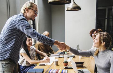 A man and a woman shake hands at a table. 