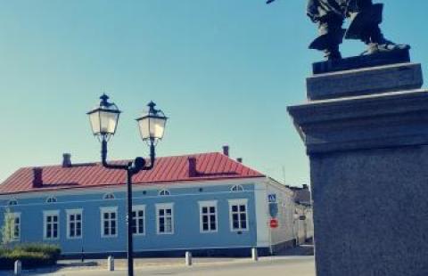 Vaaleansininen Friemanin talo Pekka-patsaan takana kesäpäivänä.