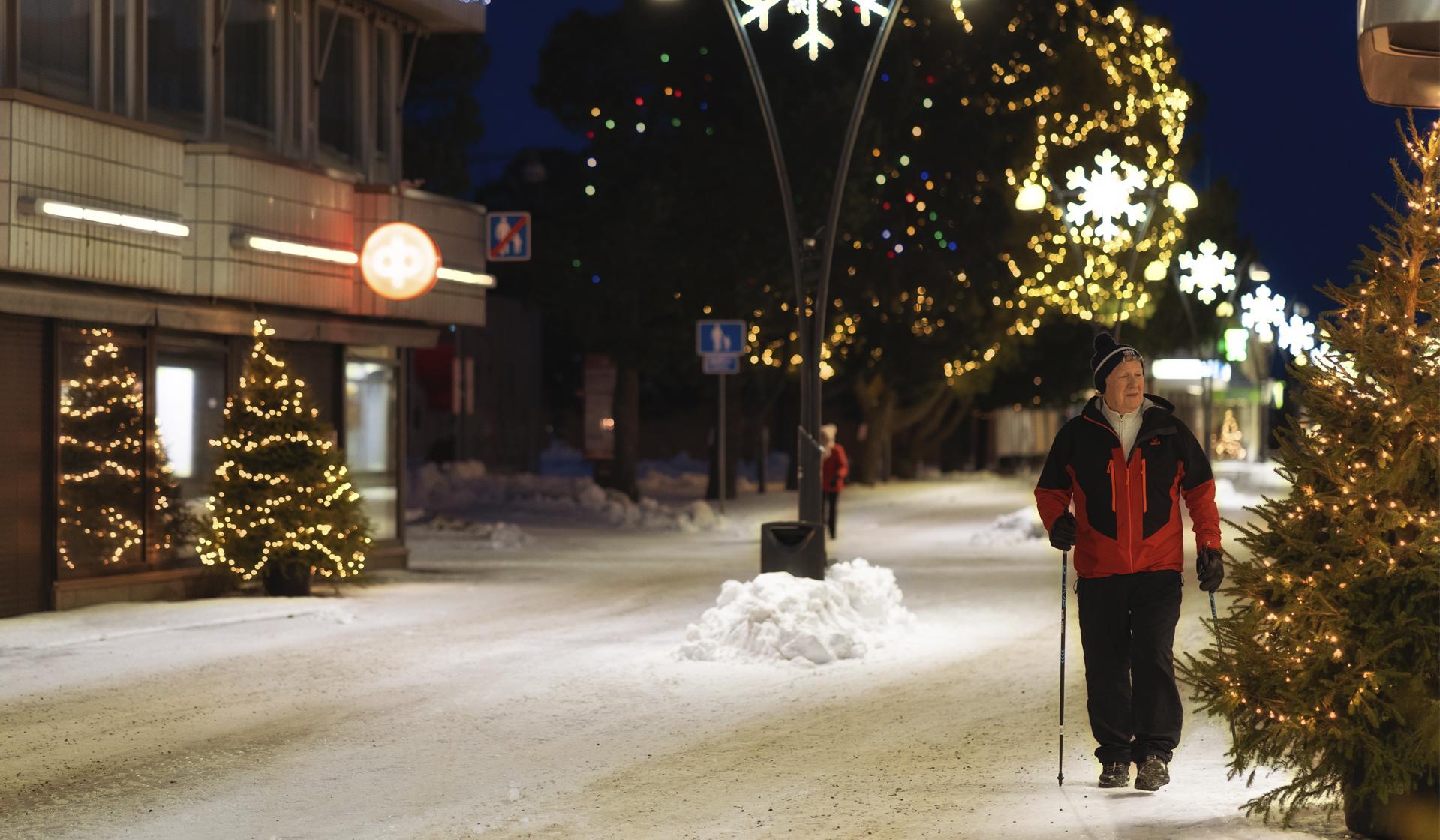 A man walking around town under the glow of Christmas lights.