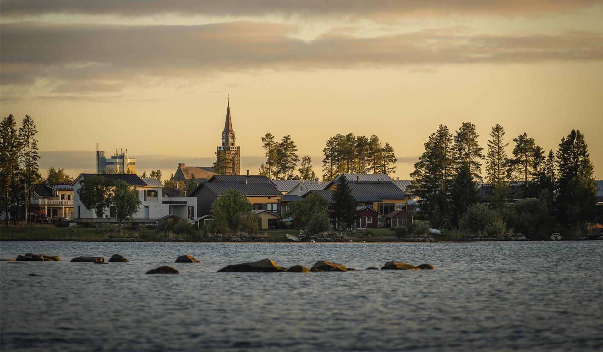 Merenrantaa, puita ja rakennuksia auringonlaskun aikaan.