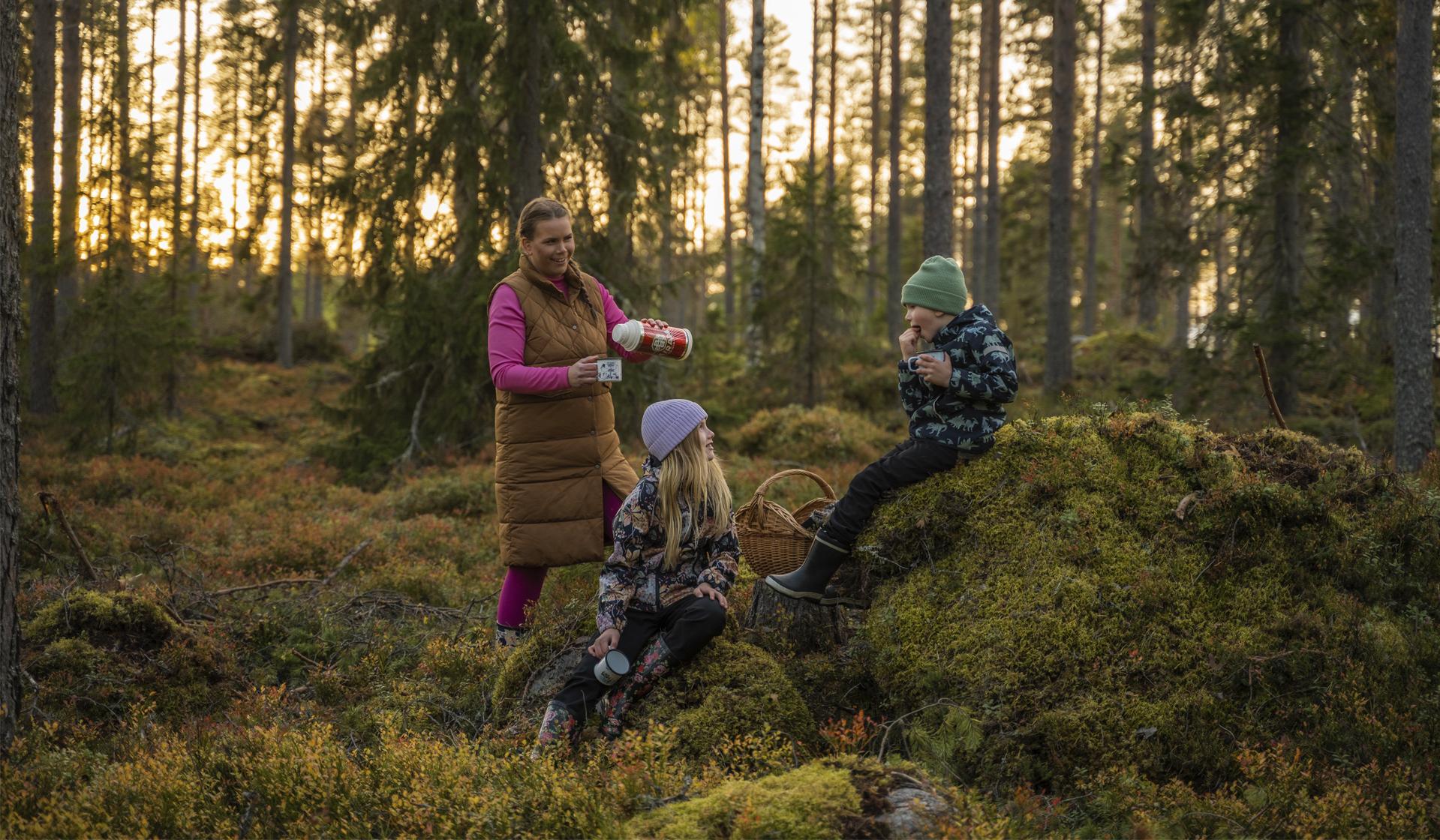 En kvinna och två barn på vandring i skogen.
