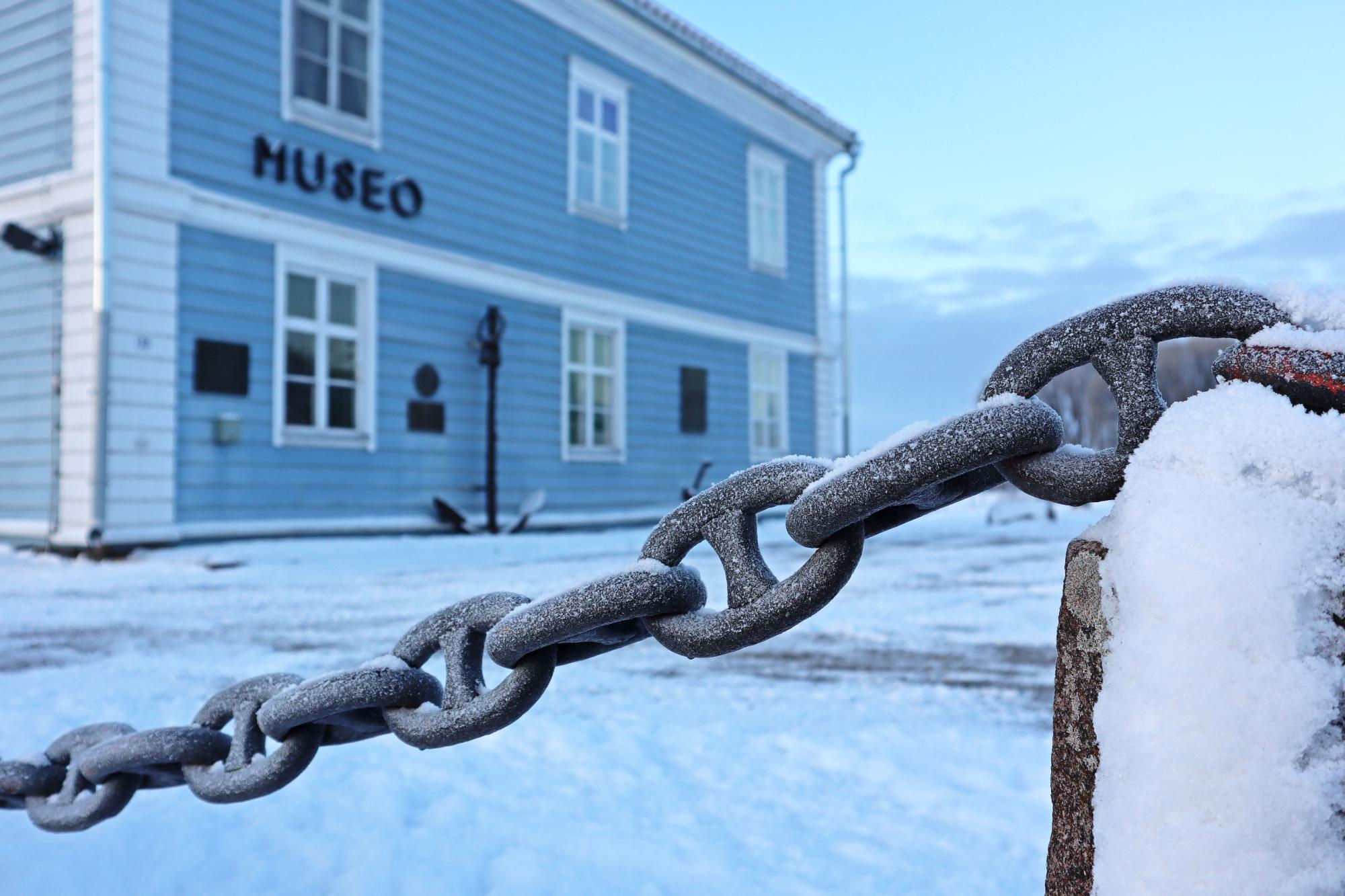 A close-up of the chain fence at the Pakkahuone Museum. The museum can be seen in the background.