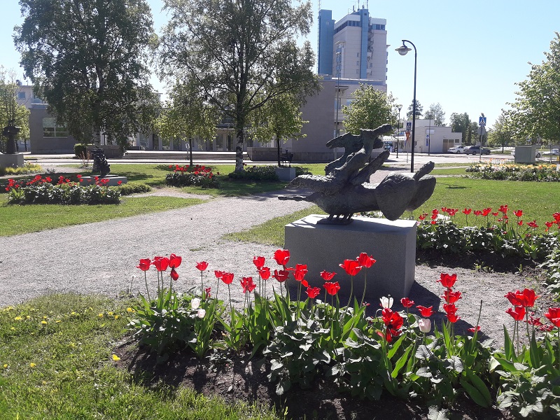 Punaiset kukat ympäröivät veistoksia puistossa.