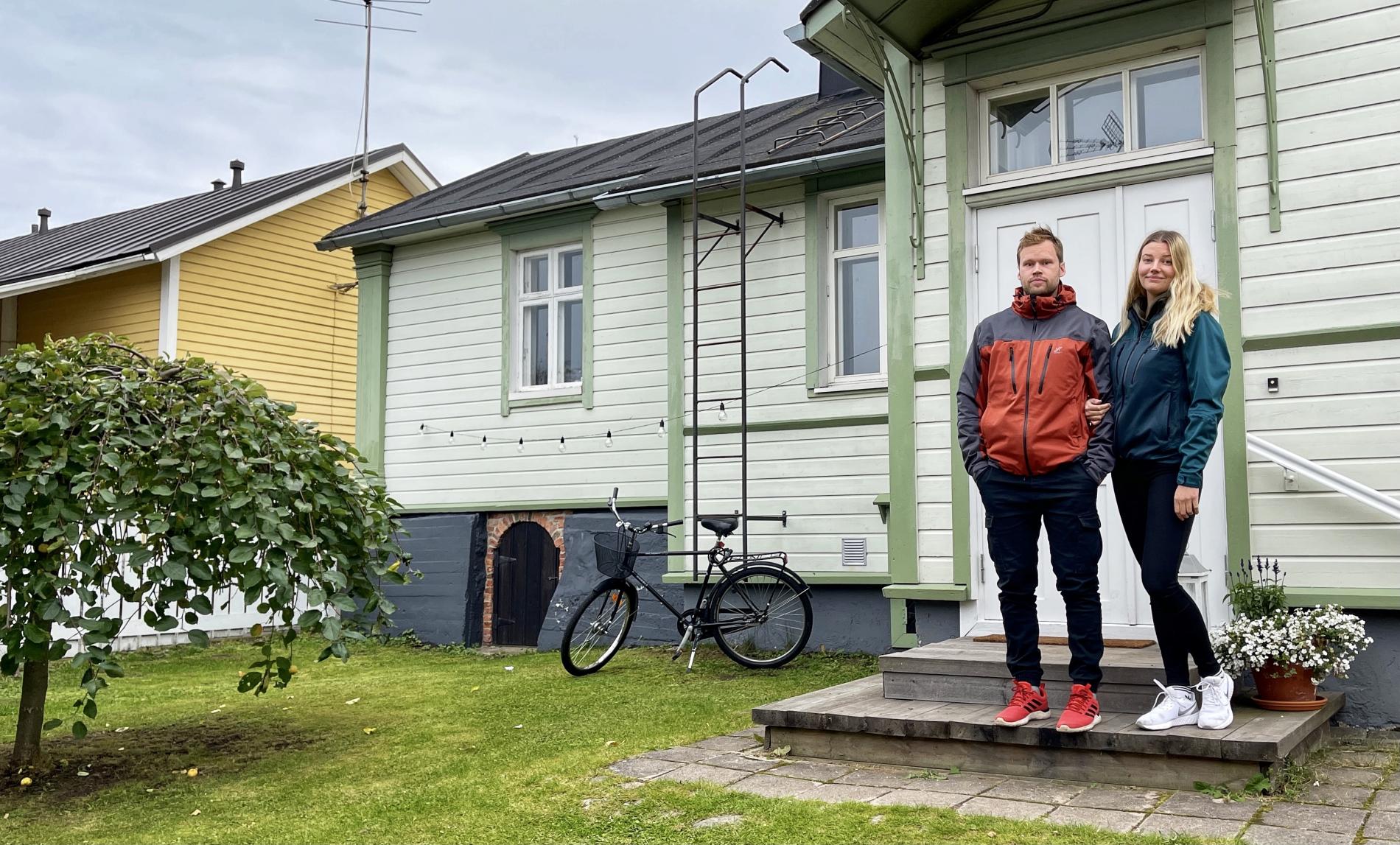 A man and a woman standing on the steps of a wooden house in the old town.