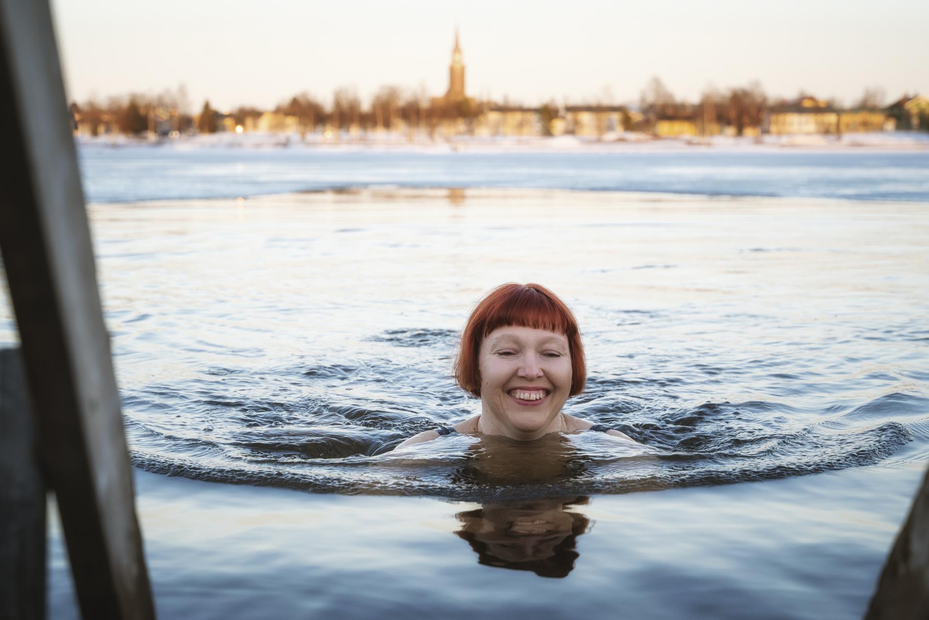 Punahiuksinen nainen avantouimassa. Taustalla Raahen kaupungin siluetti.