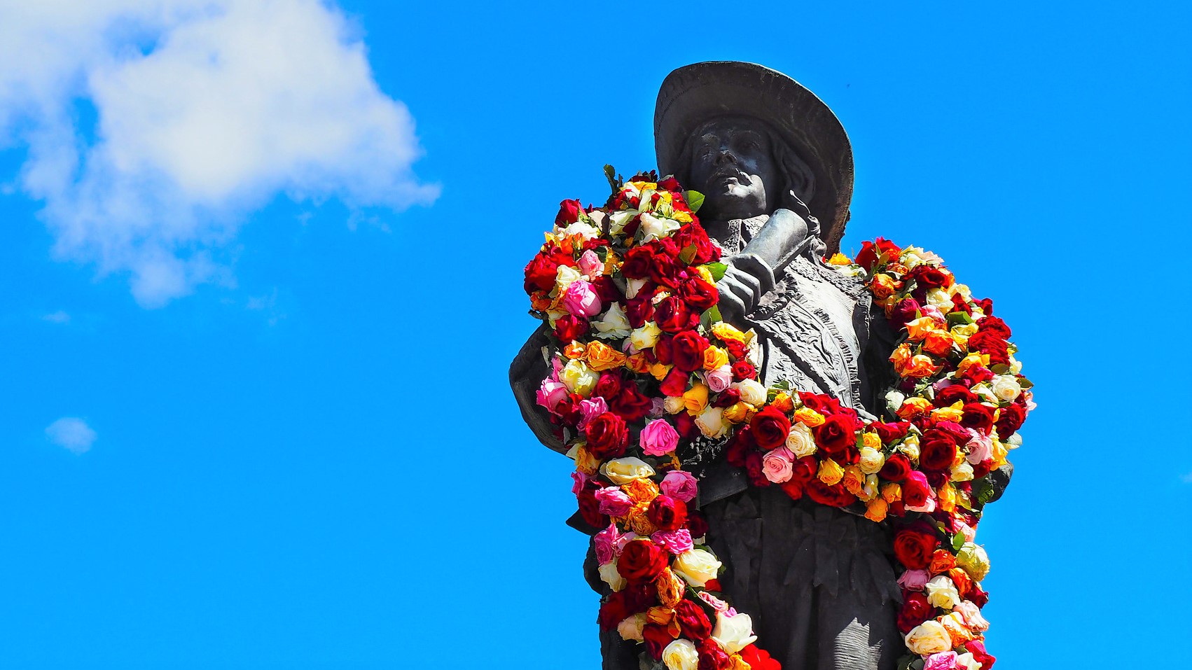 A man's statue, with large flower wreaths on his neck.